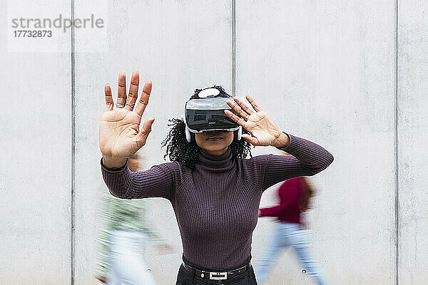 Woman wearing virtual reality simulator gesturing in front of wall