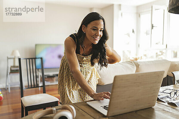 Lächelnde schwangere Frau  die von zu Hause aus mit einem Laptop arbeitet
