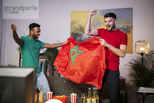 Happy football fans with Moroccan flag cheering at home