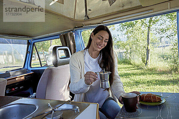 Lächelnde Frau hält Kaffeekanne neben Tasse im Wohnmobil