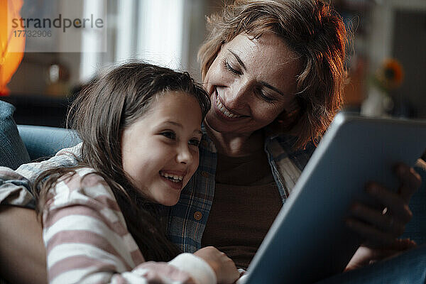 Glückliche Mutter und Tochter sitzen zu Hause mit Tablet-PC