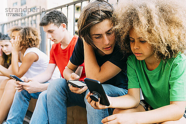 Jungen teilen sich ihr Smartphone und sitzen bei Freunden