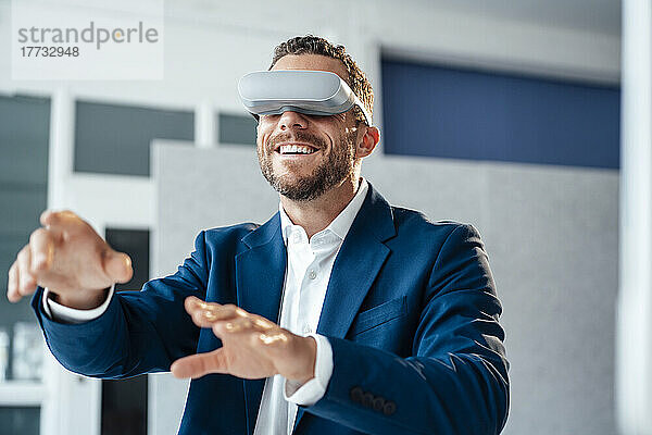 Glücklicher Geschäftsmann mit Virtual-Reality-Headset gestikuliert im Büro