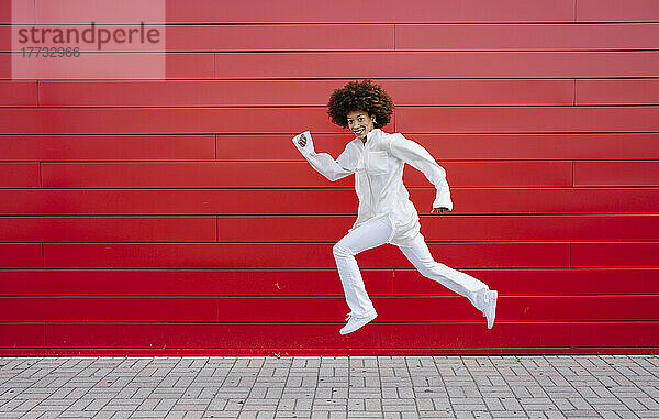 Afro-Frau springt an roter Wand vorbei