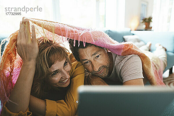 Glückliches Paar benutzt Tablet-PC  der zu Hause unter einer Decke liegt
