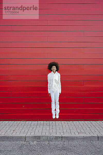Afro-junge Frau springt vor roter Wand