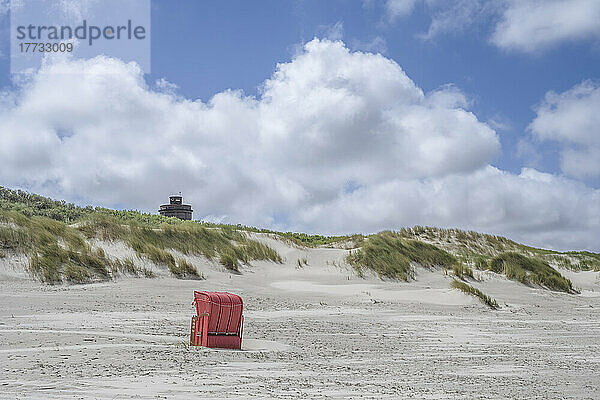 Deutschland  Niedersachsen  Juist  Strandkorb mit Kapuze am leeren Strand mit Dünen im Hintergrund