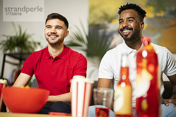 Happy young men watching football match in living room at home
