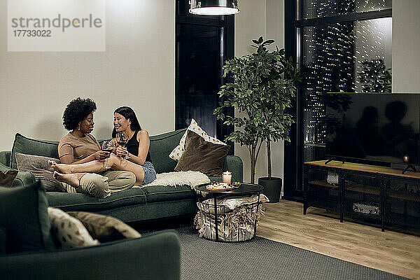 Glückliches schwules Paar  das zu Hause auf dem Sofa im Wohnzimmer sitzt und miteinander redet