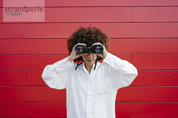 Afro-Frau schaut durch ein Fernglas vor einer roten Wand