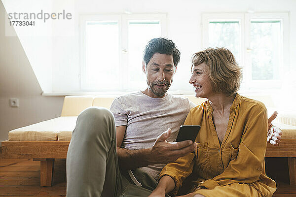 Glückliche Frau schaut Mann an  der zu Hause sein Smartphone benutzt