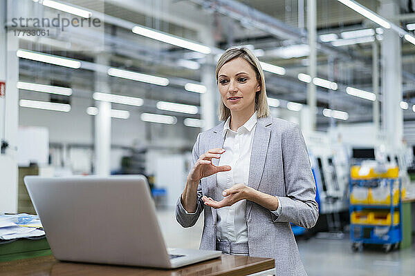 Geschäftsfrau gestikuliert während Videoanruf auf Laptop in Fabrik