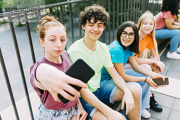 Lächelndes Teenager-Mädchen macht Selfie mit Freunden  die am Geländer sitzen