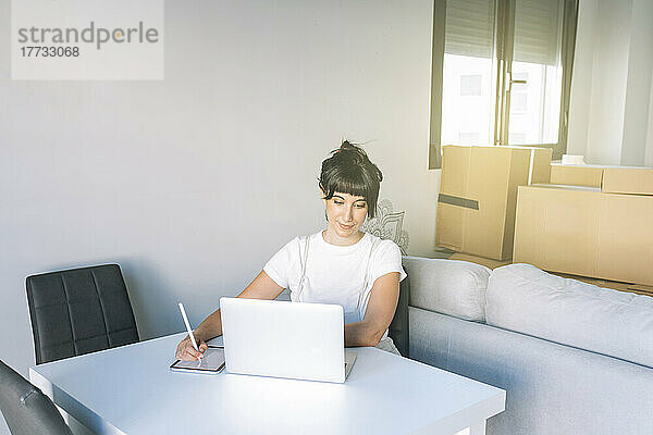 Frau mit digitalisiertem Stift und Tablet-PC blickt auf Laptop auf Tisch im Wohnzimmer