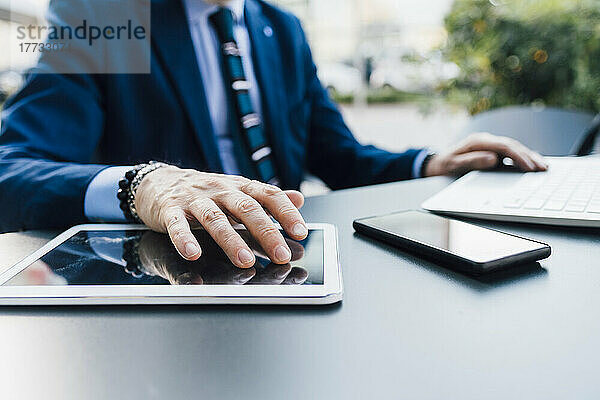 Geschäftsmann arbeitet beim Multitasking an Laptop und Tablet-PC per Smartphone am Tisch im Freien