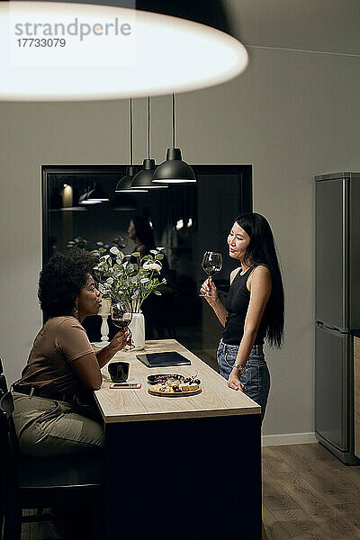 Freundinnen mit Weingläsern reden zu Hause in der Küche miteinander