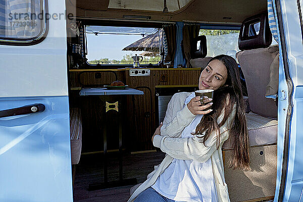 Frau mit Kaffeetasse träumt vor der Tür des Wohnmobils