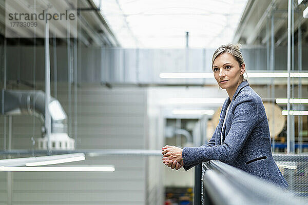 Businesswoman leaning on railing in factory