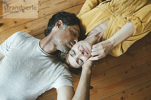Man kissing woman with eyes closed lying on floor at home