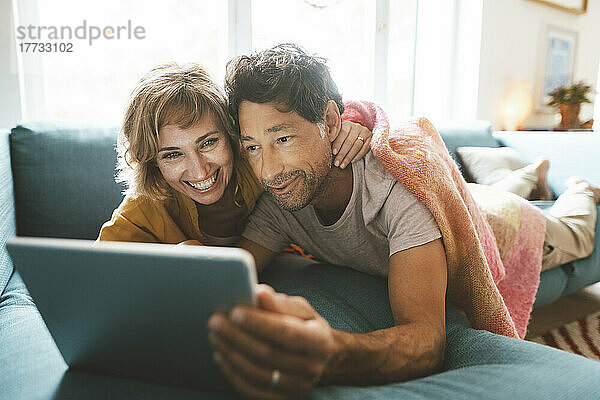 Glückliches älteres Paar mit Tablet-PC  das zu Hause auf dem Sofa liegt