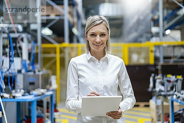 Porträt einer lächelnden Geschäftsfrau mit digitalem Tablet in der Fabrik