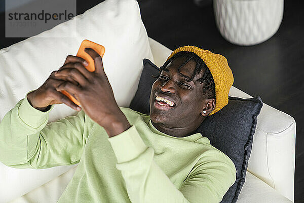 Happy man using smart phone lying on sofa at home