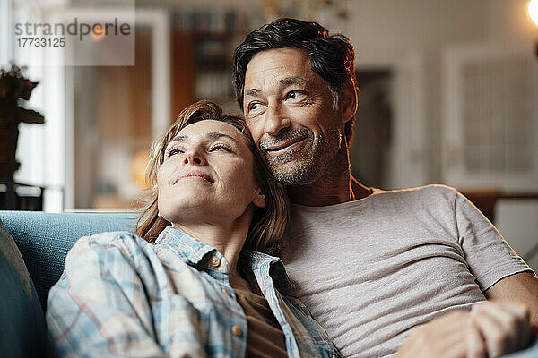 Lächelnde reife Frau mit Mann  der zu Hause auf dem Sofa sitzt