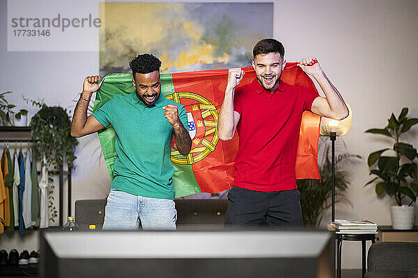 Fröhliche junge Männer mit portugiesischer Flagge genießen das Fußballspiel zu Hause