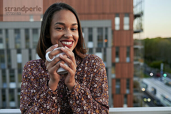 Happy young woman with coffee cup in front of building