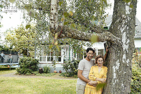 Glückliches Paar steht am Baum vor dem Haus