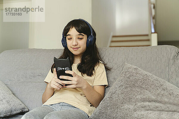 Mädchen hört Musik und benutzt Smartphone im Wohnzimmer