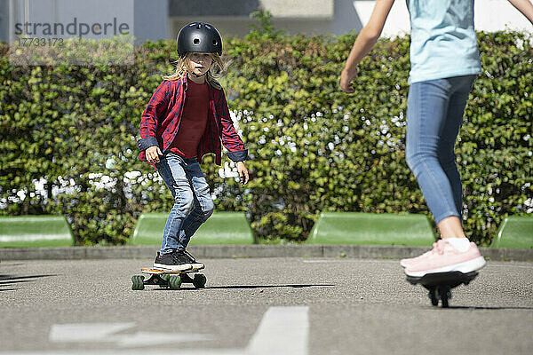 Boy wearing helmet skateboarding with friend on traffic course