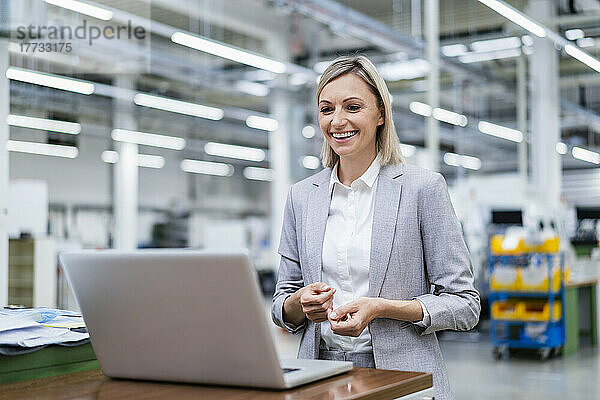 Glückliche Geschäftsfrau schaut in der Fabrik auf Laptop