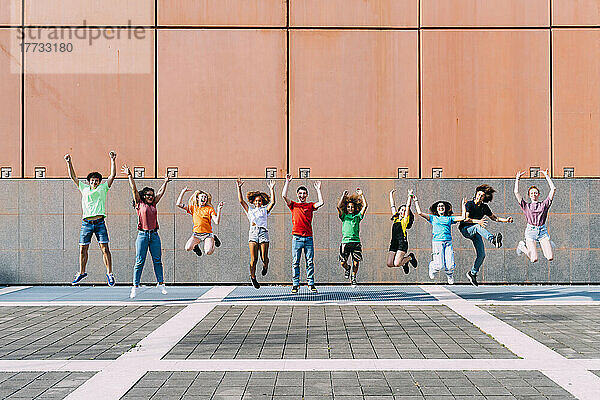 Fröhliche Freunde springen an einem sonnigen Tag vor die Wand