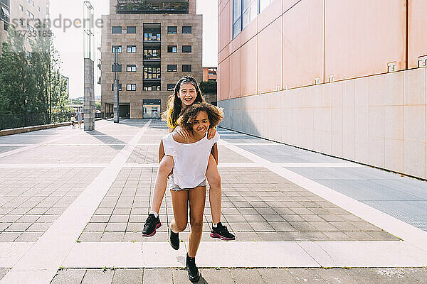 Smiling girl giving piggyback ride to friend on sunny day