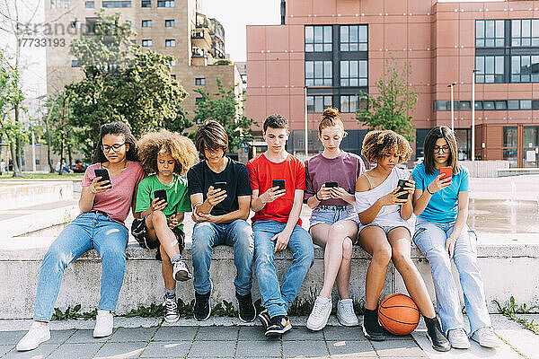 Gruppe von Freunden  die Smartphones benutzen und an der Wand sitzen