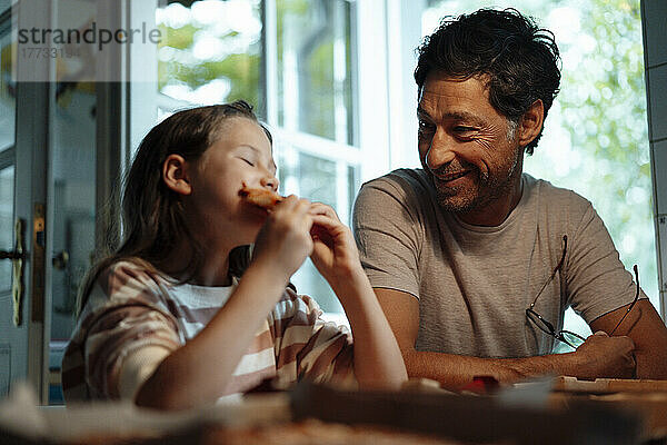 Lächelnder Mann schaut seiner Tochter beim Essen zu Hause zu