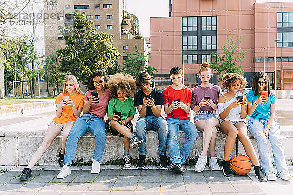 Freunde  die Smartphones benutzen  sitzen an der Wand