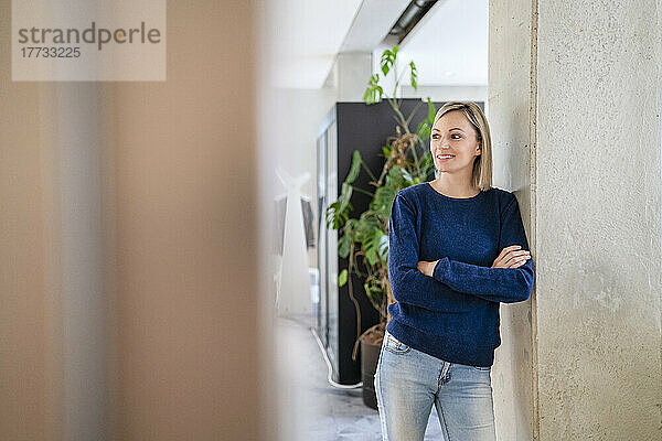 Smiling businesswoman leaning against column in office