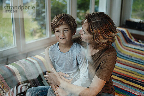 Lächelnde Frau mit Sohn sitzt zu Hause auf dem Sofa