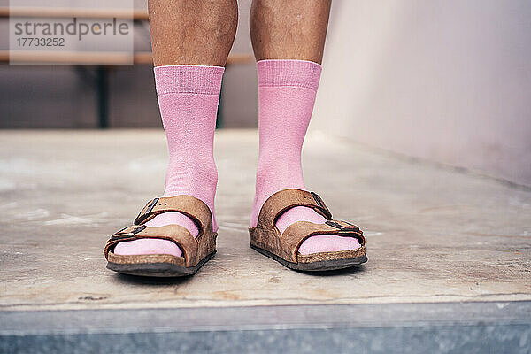 Beine eines Mannes  der auf dem Boden steht und rosa Socken und Sandalen trägt