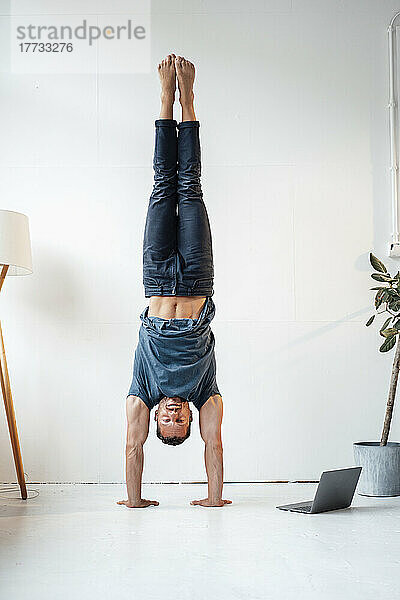 Reifer Mann übt zu Hause Handstand vor der Wand