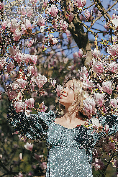 Blonde Frau steht an einem sonnigen Tag inmitten rosa Blumen