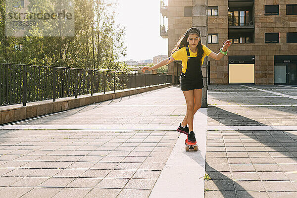 Mädchen fährt an einem sonnigen Tag vor dem Gebäude Skateboard