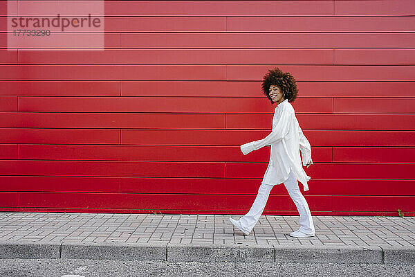 Lächelnde Frau  die auf dem Bürgersteig an einer roten Wand läuft