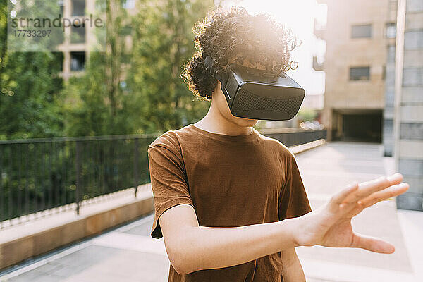 Junge trägt einen Virtual-Reality-Simulator und gestikuliert an einem sonnigen Tag
