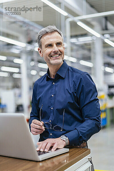 Lächelnder Geschäftsmann mit Laptop in der Fabrik