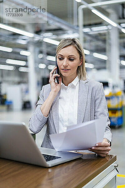 Geschäftsfrau mit Laptop am Telefon in der Fabrik