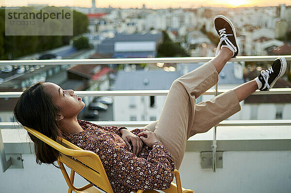 Nachdenkliche junge Frau entspannt sich auf einem Stuhl auf dem Balkon