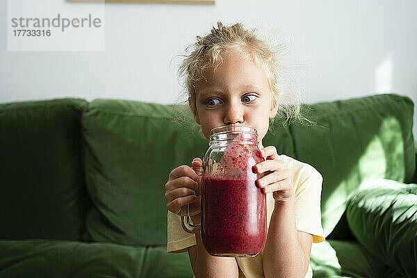 Mädchen trinkt hausgemachten Erdbeer-Smoothie im Wohnzimmer